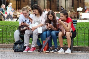 dzieci siedza na lawce z telefonami
